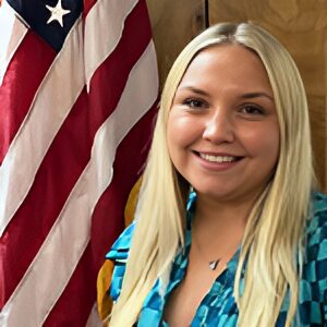 Smiling person in front of American flag.