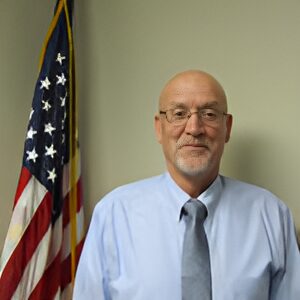 Man in shirt and tie, American flag background.
