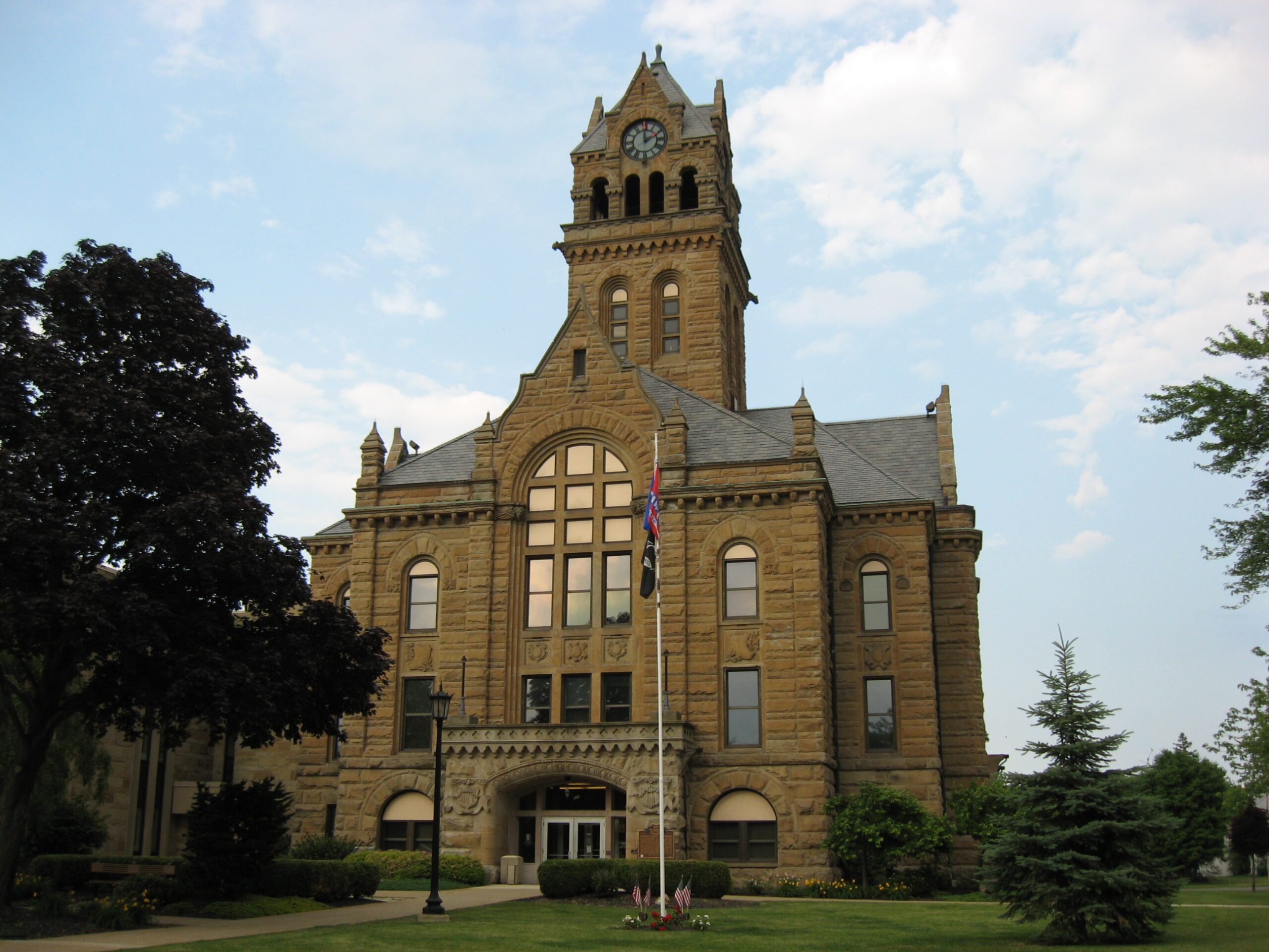 Ottawa County Courthouse stone, three-story structure with clock tower. Grass and flag pole in forefront with blue sky.