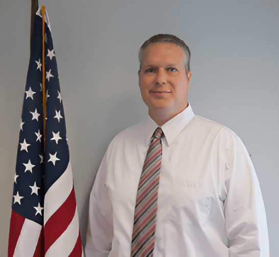 Man in white shirt near American flag.