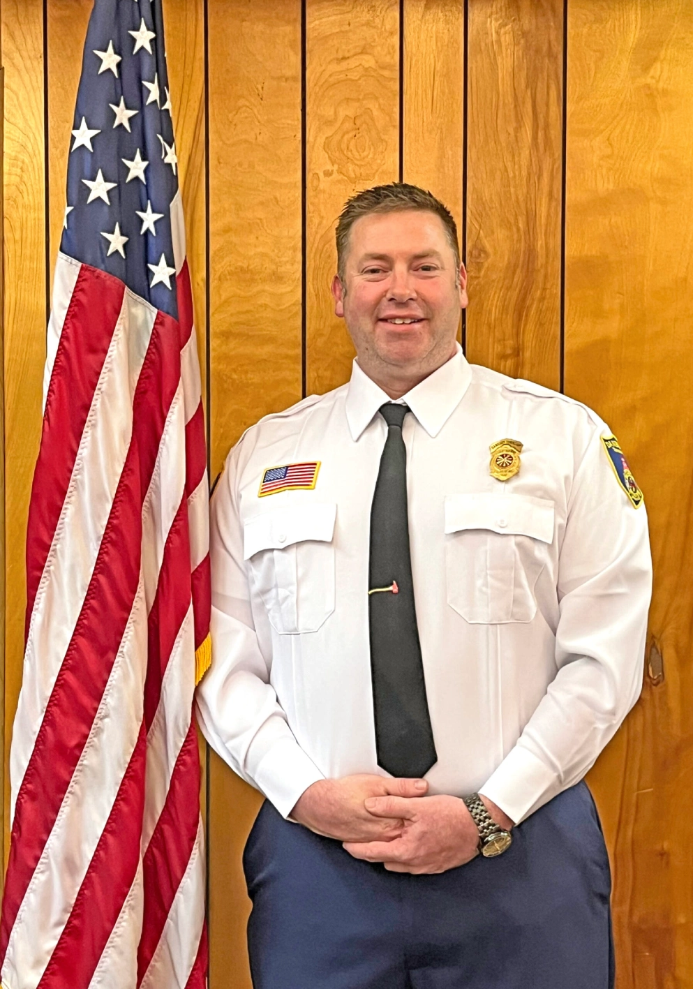 Uniformed man standing beside American flag.