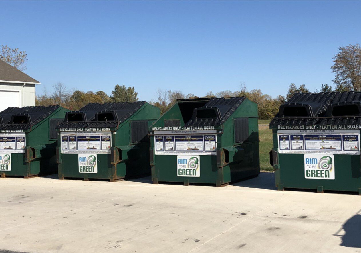 Four green recycling dumpsters in a row.